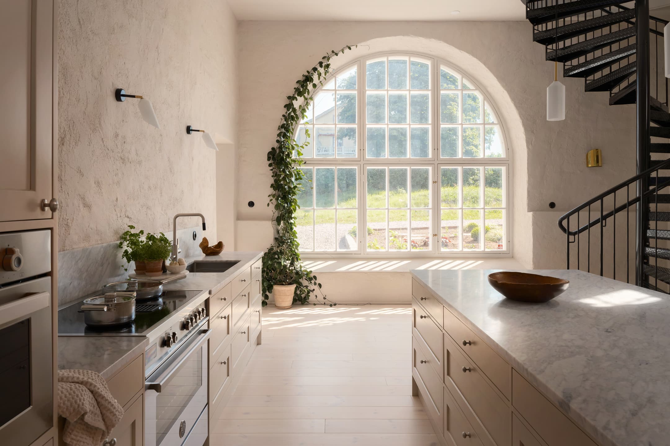Range cooker in a bright kitchen with marble worktops, beige cabinets and a large arched window