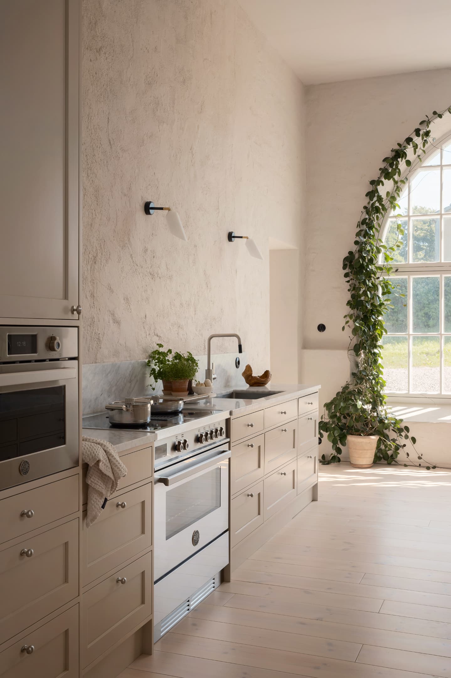 LSBolagen case: range cooker, built-in oven and beige cabinets in a kitchen with a large arched window